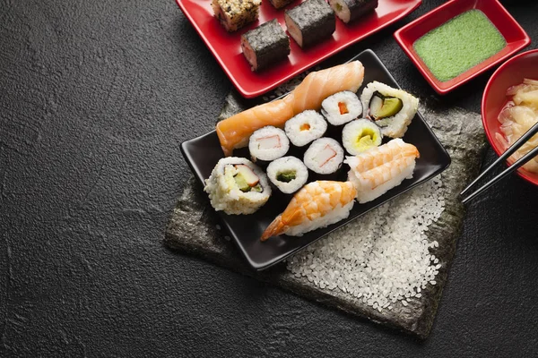 Sushi definido em pratos vermelhos e pretos e fundo de mesa preta — Fotografia de Stock