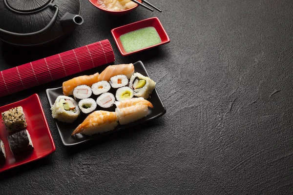 Conjunto de sushi e bule preto na mesa preta — Fotografia de Stock