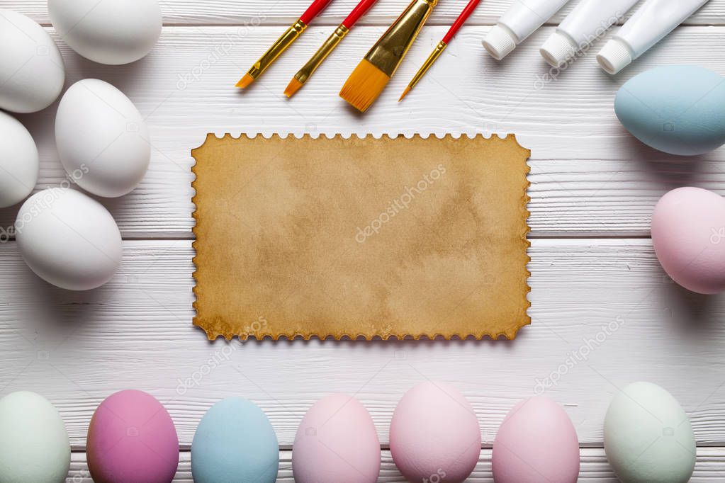 Painting Easter eggs - brushes, paints, eggs and blank paper sheet on white wooden planks