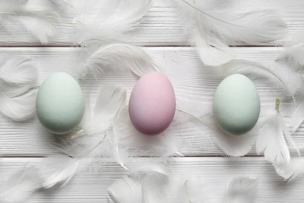 三彩色鸡蛋和白色羽毛在木桌上 — 图库照片