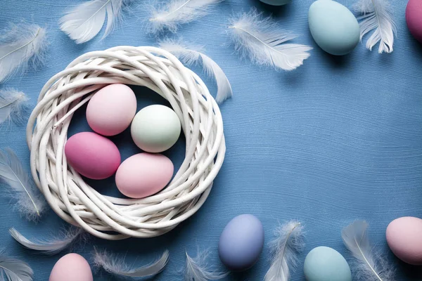Plumas y huevos de Pascua de colores en el nido y fondo azul —  Fotos de Stock