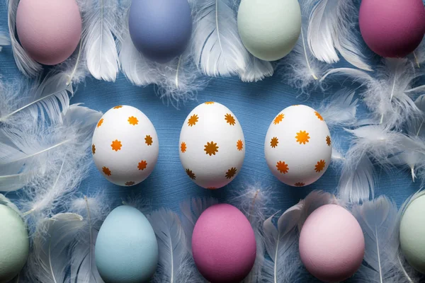 Witte en gekleurde paaseieren en witte veren op blauw backgro — Stockfoto