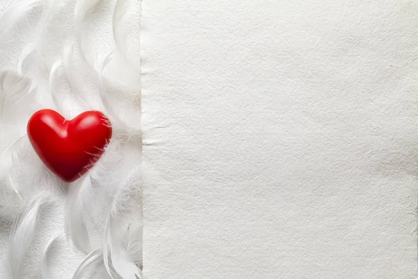 Um coração vermelho, penas e folha de papel artesanal branca — Fotografia de Stock