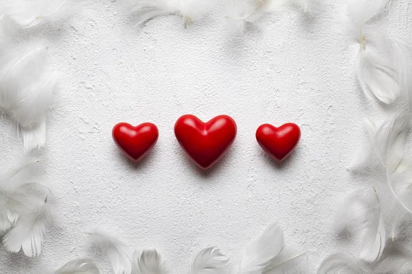 Tres pequeños corazones rojos y plumas sobre fondo enlucido blanco — Foto de Stock