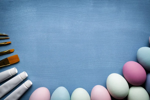 Uova di Pasqua dipinte, pennelli e vernici su sfondo blu — Foto Stock