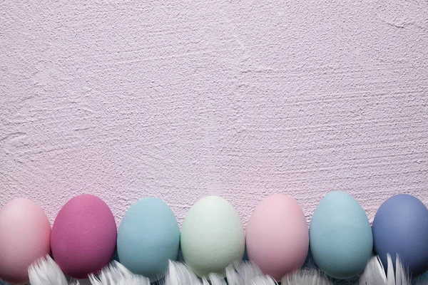 Colored Easter eggs and feathers on pink plastered wall backgrou