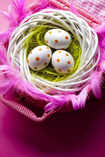 Три розмальовані великодні яйця в гнізді і рожевий кошик — стокове фото