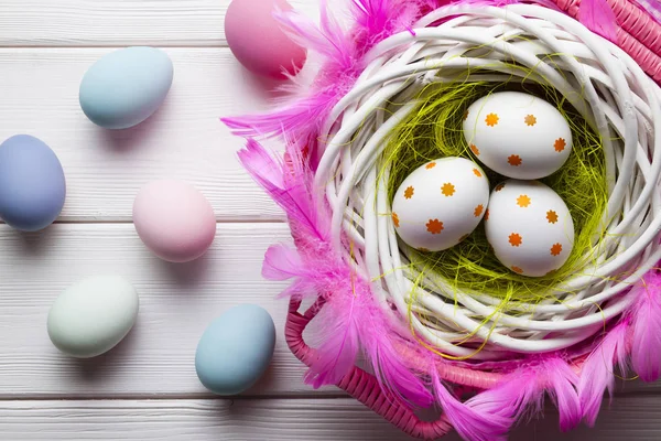 Witte en gekleurde paaseieren in mand en witte houten achterop — Stockfoto