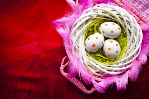 Três ovos de Páscoa brancos no ninho no fundo vermelho — Fotografia de Stock