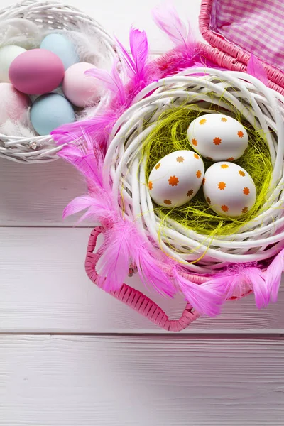 Uova di Pasqua bianche e colorate in cesto su backgrou di legno bianco — Foto Stock