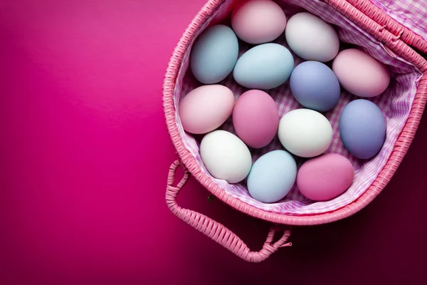 Pasen-achtergrond - gekleurde eieren in een mand op roze achtergrond — Stockfoto