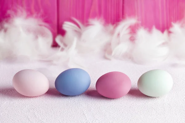 Quattro uova di Pasqua colorate e piume bianche sul dorso in legno rosa — Foto Stock