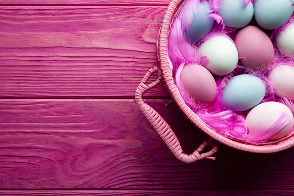 Huevos y plumas de Pascua de colores en cesta sobre fondo de madera rosa —  Fotos de Stock