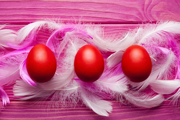 Pasen-achtergrond - gekleurde eieren en veren op roze houten bac — Stockfoto