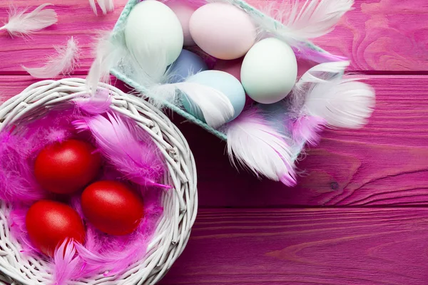 Colored Easter eggs, feathers and baskets on pink wooden backgro