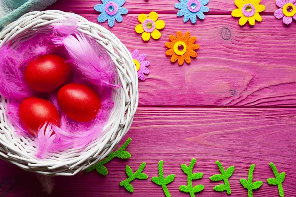 Ovos de Páscoa coloridos, penas e outras decorações em madeira rosa — Fotografia de Stock