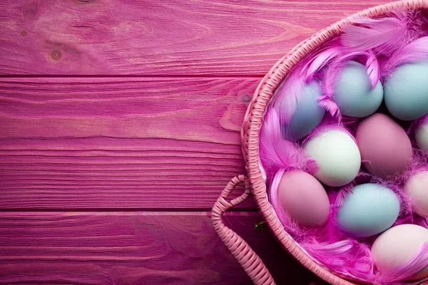 Pasen-achtergrond - gekleurde eieren en veren in de mand op woode — Stockfoto