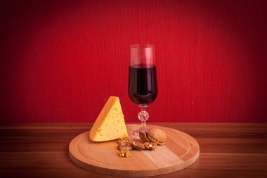 Peynirli kırmızı şarap kadehi, koyu kırmızı arka planda fındık.
