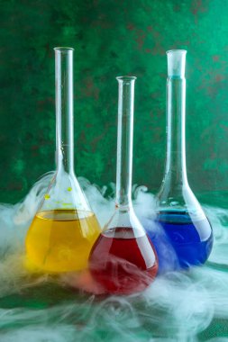 Renkli sıvı ile cam test tüpleri ve yeşil arka planda duman