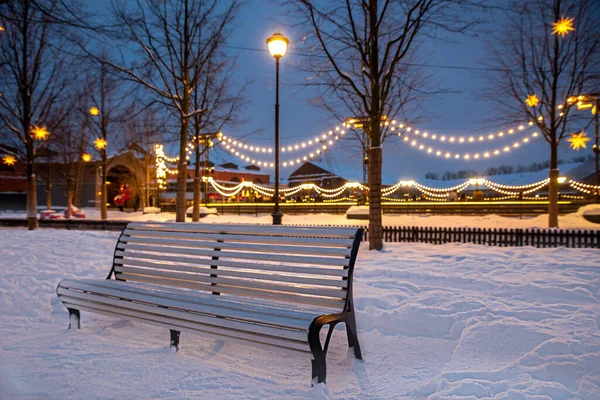 empty brench in a winter park with lights at background