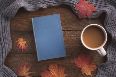 Sonbahar, rahat kompozisyon. Sıcak atkı, kitap, bir fincan kahve, ahşap zemin üzerinde akçaağaç yaprakları. Düz konum, üst görünüm, kopyalama alanı.