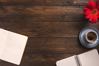 Cozy workplace. Open notebooks, cup of coffee, flower, on wooden background. Flat lay, top view, copy space.