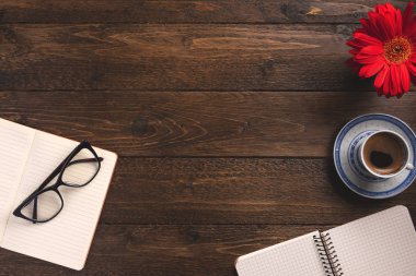 Cozy workplace. Open notebooks, cup of coffee, flower, on wooden background. Flat lay, top view, copy space.