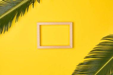 Palm leaves and photo frame, on yellow background. Top view, copy space. Flat lay.