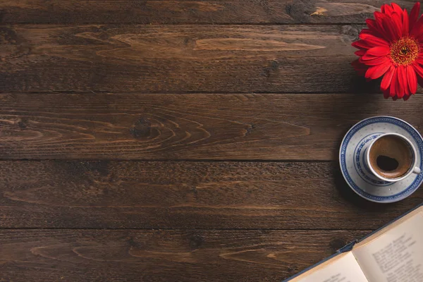 Open book, cup of coffee, flower, on wooden background. Flat lay, top view, copy space.