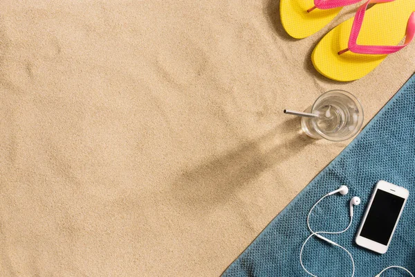 夏休みの構成 砂の背景に水のフリップフロップ スマートフォンやガラス 影の強い光 夏の背景 タオル製のボーダー構成 — ストック写真