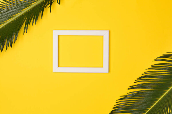 Palm leaves and photo frame, on yellow background. Top view, copy space. Flat lay.