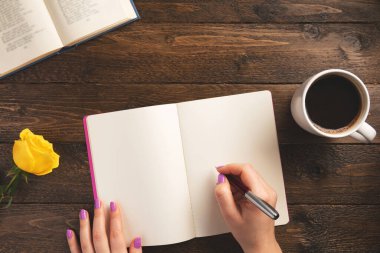 Dişi el kalem. Not defteri, bir fincan kahve, gül, ahşap arka planda. Düz konum, üst görünüm, kopyalama alanı.