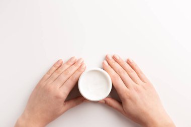 Bakım kozmetik konsepti. Beyaz arka planda izole edilmiş kozmetik krem kabını tutan kadın eller. Düz konum, üst görünüm, kopyalama alanı.