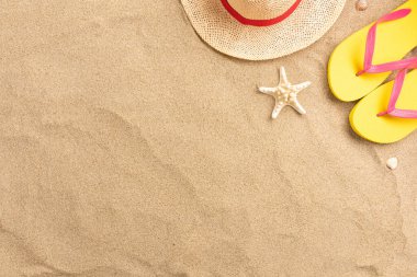 Parmak arası terlik, hasır şapka, kumlu arka plan. Plaj tatili konsepti. Fotokopi alanı olan top view.