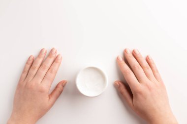 Beyaz arka planda, izole edilmiş krema kabı olan kadın elleri. Düz konum, üst görünüm, kopyalama alanı. Organik kozmetik konsepti.