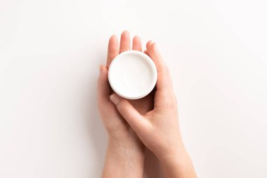 Beyaz arka planda, izole edilmiş krema kabı olan kadın eller. Düz konum, üst görünüm, kopyalama alanı. Organik kozmetik konsepti.