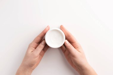 Bakım kozmetik konsepti. Beyaz arka planda izole edilmiş kozmetik krem kabını tutan kadın eller. Düz konum, üst görünüm, kopyalama alanı.