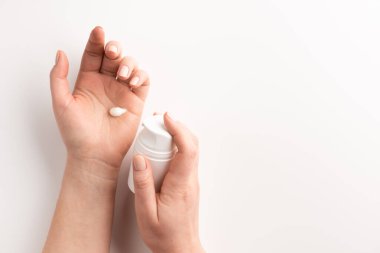 Bakım kozmetik konsepti. Beyaz arka planda izole edilmiş kozmetik krem konteynırı tutan bir kadın. Düz konum, üst görünüm, kopyalama alanı.