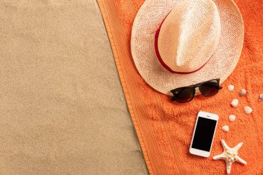 Yaz modası, kumlu arka planda yaz kıyafeti. Akıllı telefon, güneş gözlüğü ve hasır şapka. Düz yatış, üst görünüm
