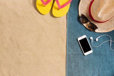 Yaz tatili kompozisyonu. Şapka, akıllı telefon ve kumsalda güneş gözlüğü. Gölgeli sert bir ışık. Yaz dönemi. Havludan yapılmış kenar bileşimi