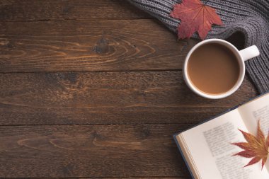 Düz bir kompozisyon, örgü eşarp, bir fincan kahve, kitap ve ahşap masa üzerinde sarı yapraklar. Hygge tarzı, sıcak sonbahar ya da kış tatili konsepti. Düz yatıyordu, üstten, yukarıdan..