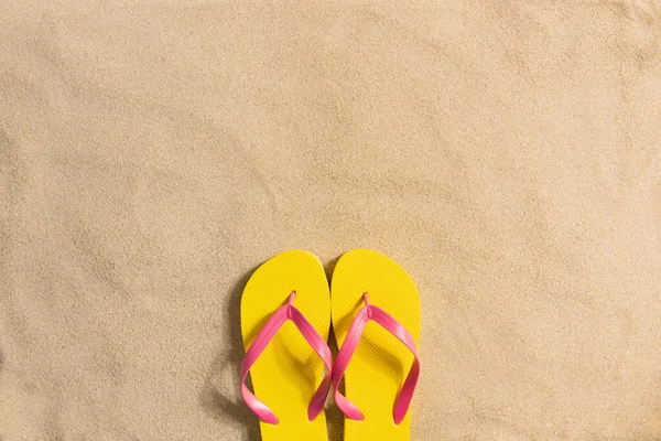 Summer fashion, summer outfit on sand background. Yellow flip flops aon the sand. Flat lay, top view