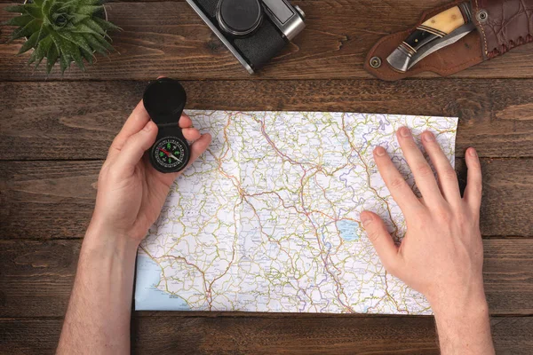 Travel planning concept. Hands holding compass with knife, vintage camera and map on wooden table background.