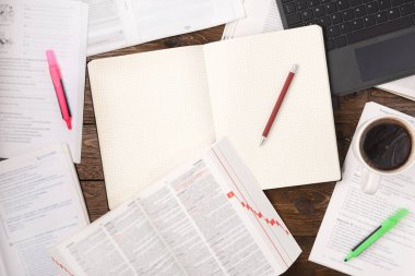 Uzaktan eğitim konsepti. Açık kitaplar, akıllı telefon, dizüstü bilgisayar, bir fincan kahve ve tahta arka planda boş not defteri. Düz konum, ofis çalışma alanı