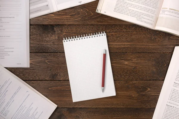 Remote education concept. Open books and blank notepad with a pen on wooden desk, flat lay