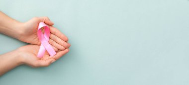 Pink ribbon in hands on turquoise background. National cancer survivor day.