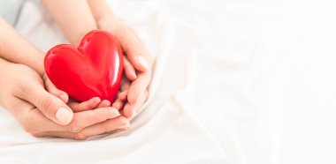 An adult, mother and child hold a red heart in their hands. Concept for charity, health insurance, love, international cardiology day.