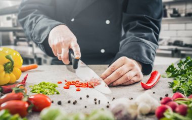 The chef in a black apron prepares the dish. Chopping vegetables in the kitchen.