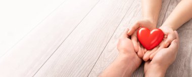Yetişkin, anne, baba ve çocuk ellerinde kırmızı bir kalp tutuyor. Yardım, sağlık sigortası, aşk, uluslararası kardiyoloji günü kavramı.