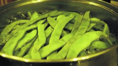 İçinde kaynar yeşil fasulye kabukları olan büyük metal tavanın tepesi.